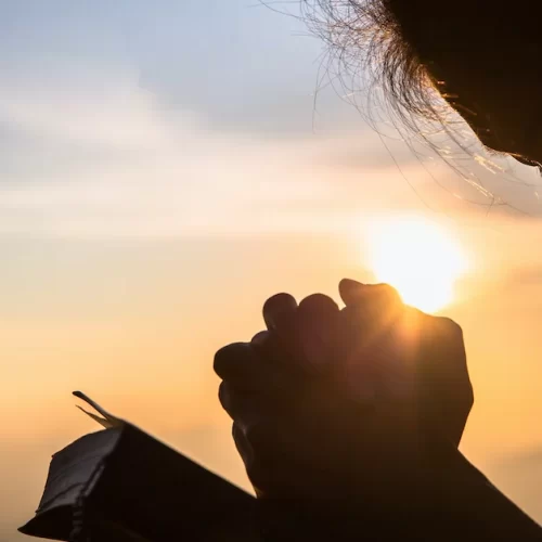 Silhouette of christian young woman praying with a  cross and open the bible at sunrise, Christian Religion concept background.