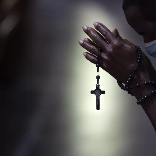 With rosary beads wrapped around clasped hands, a man bows in prayer during a Mass at the Metropolitan Cathedral, in Rio de Janeiro, Brazil, Saturday, July 4, 2020. Following an easing of restrictions related to COVID-19, the Catholic church in Rio celebrated its first Mass with 30% of its worshippers, while observing preventive measures to avoid spreading the new coronavirus. (AP Photo/Leo Correa)